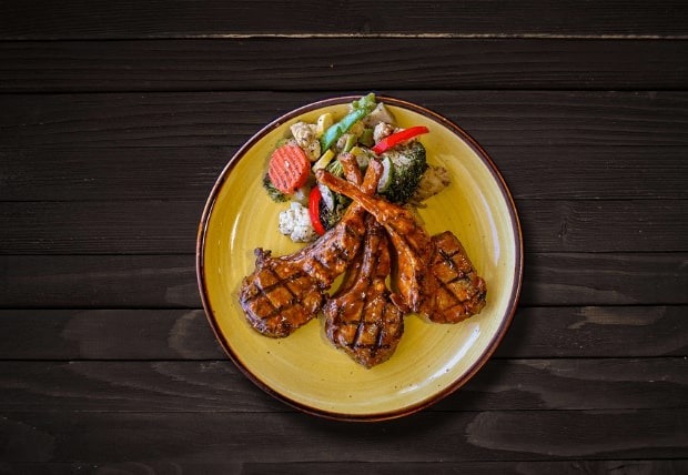 Three flame-grilled Zabiha Halal peri lamb chops served with vegetables on a plate at La Peri Peri in Sterling Heights