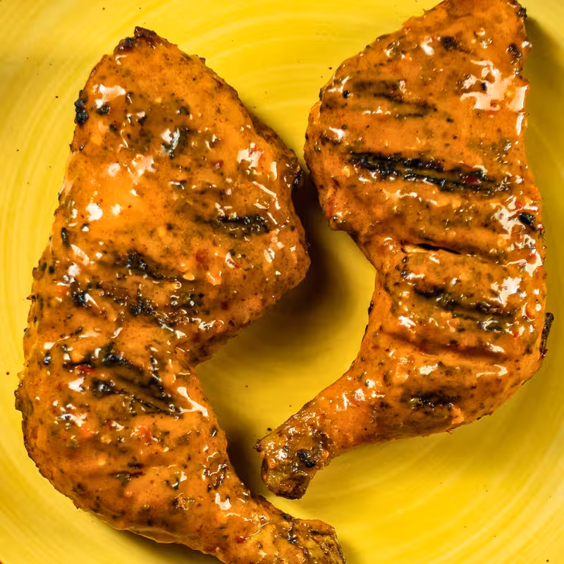 Two flame-grilled chicken leg quarters with seasoned rice on a plate at La Peri Peri in Sterling Heights, Michigan