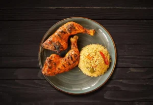 Two flame-grilled chicken leg quarters with seasoned rice on a plate at La Peri Peri in Sterling Heights, Michigan